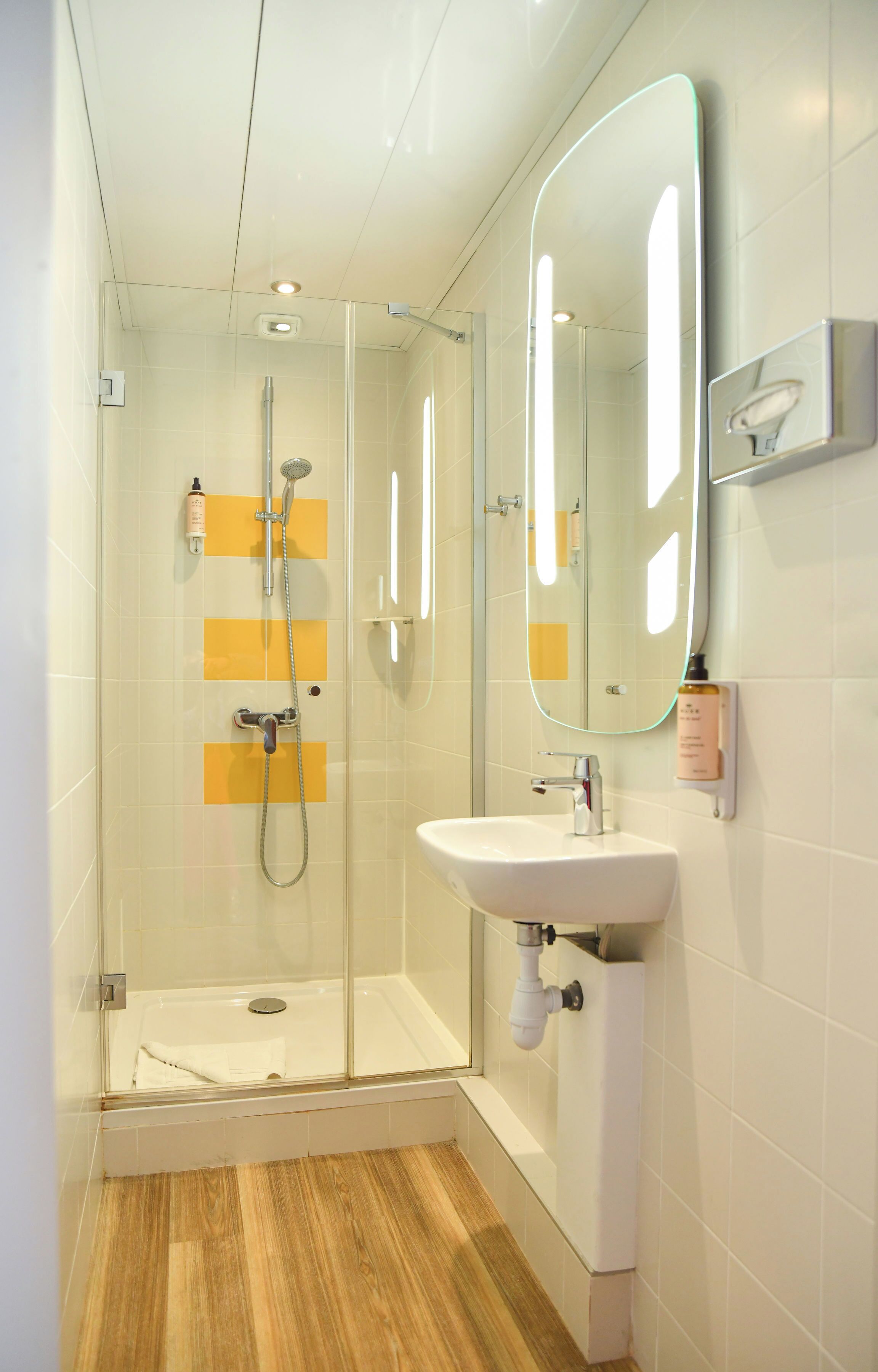 A modern bathroom with a glass-enclosed shower, a white sink, and a mirror with built-in lighting.