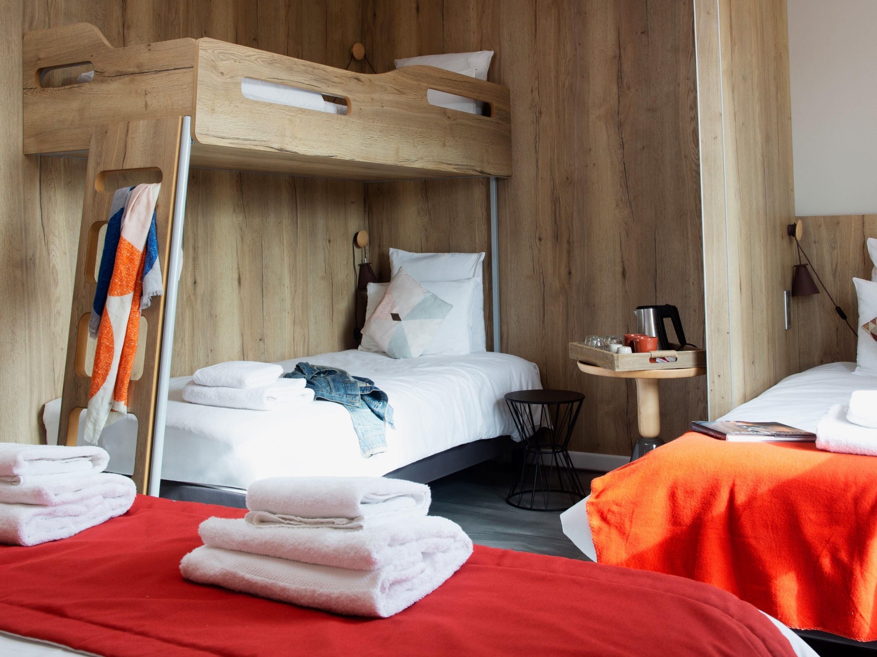 A bunk bed room with a wooden headboard, a small side table with a lamp, and a red bedspread.