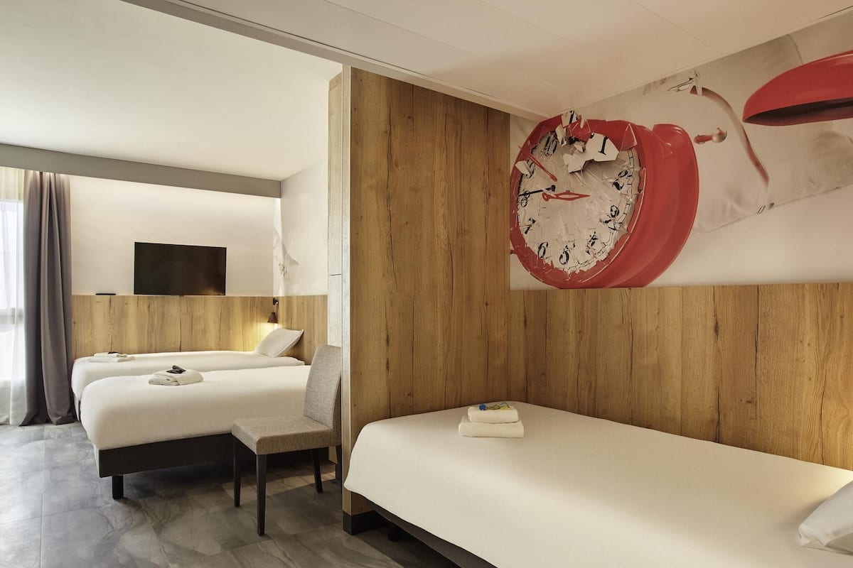 A hotel room with two beds, a wooden headboard, a large wall clock, and a flat-screen TV.