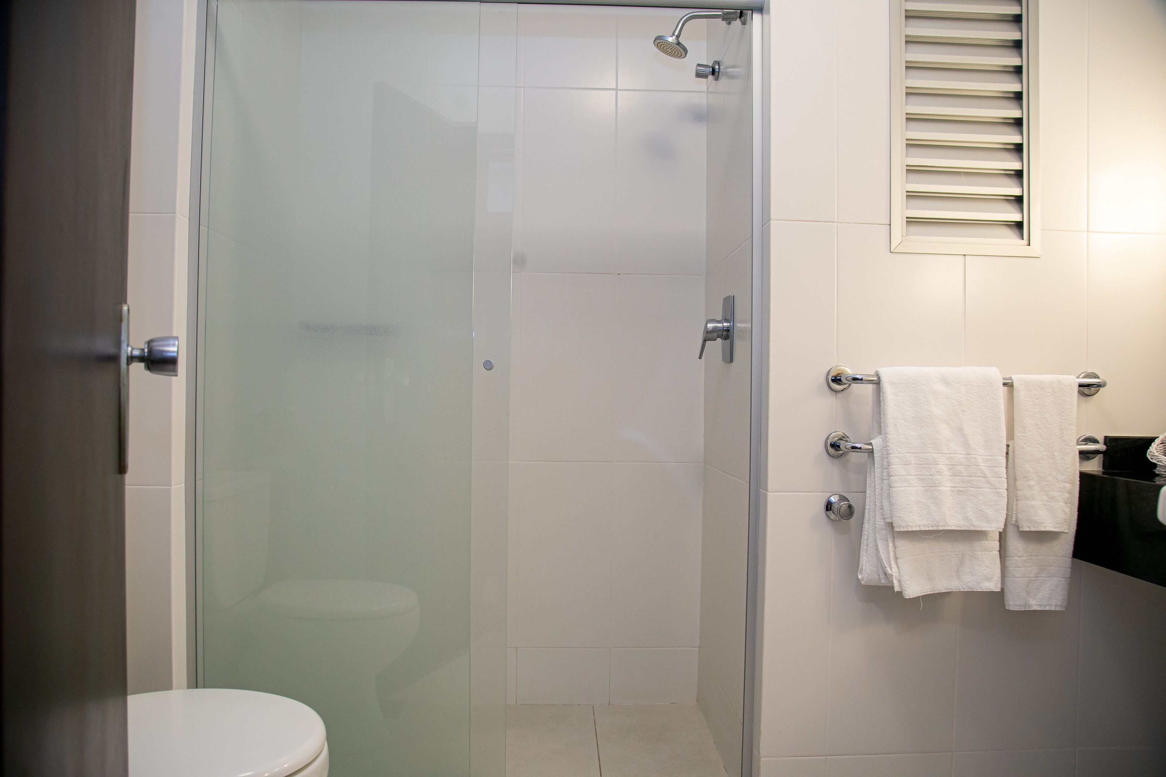 A bathroom with a glass-enclosed shower, a toilet, and a sink with a towel rack.