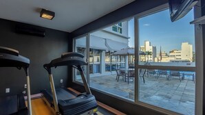Un gimnasio con cintas de correr y vistas a un paisaje urbano a través de amplios ventanales.