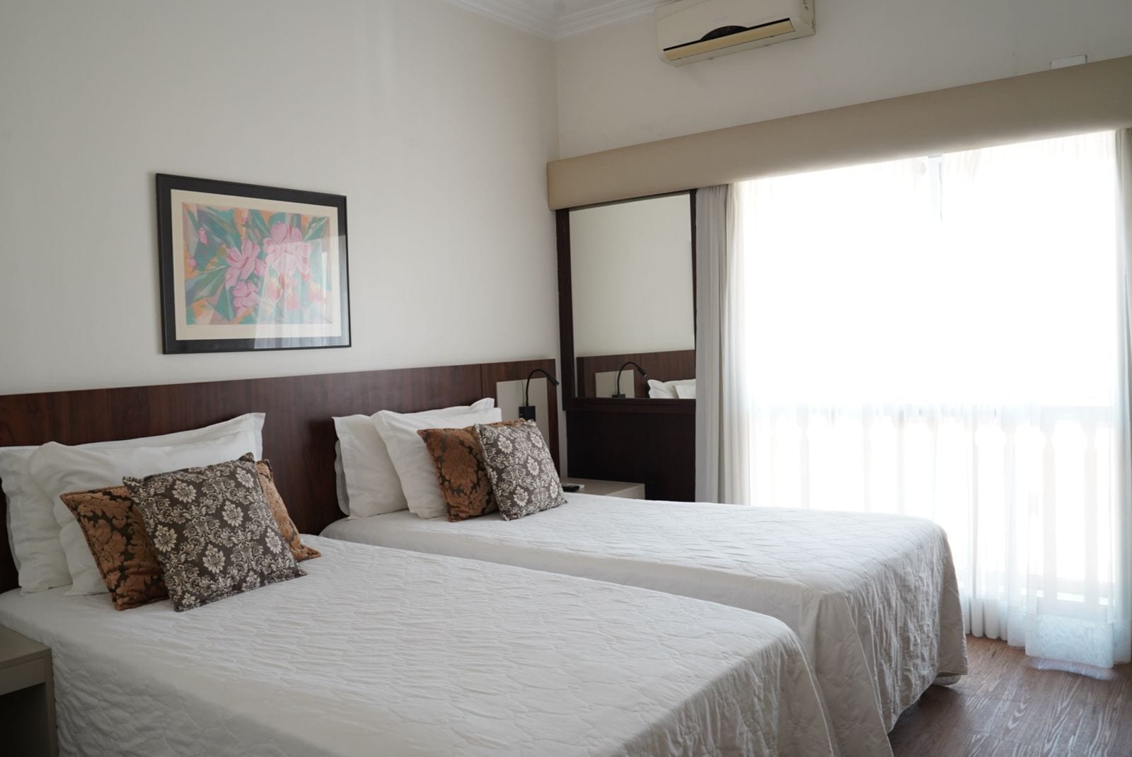 Habitación de hotel con dos camas, un espejo grande y un balcón con cortinas.