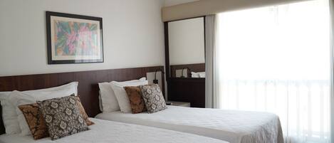 Habitación de hotel con dos camas, un espejo grande y un balcón con cortinas.