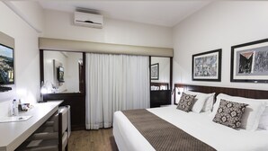 Habitación de hotel con cama, escritorio, silla, espejo y ventana con cortinas.