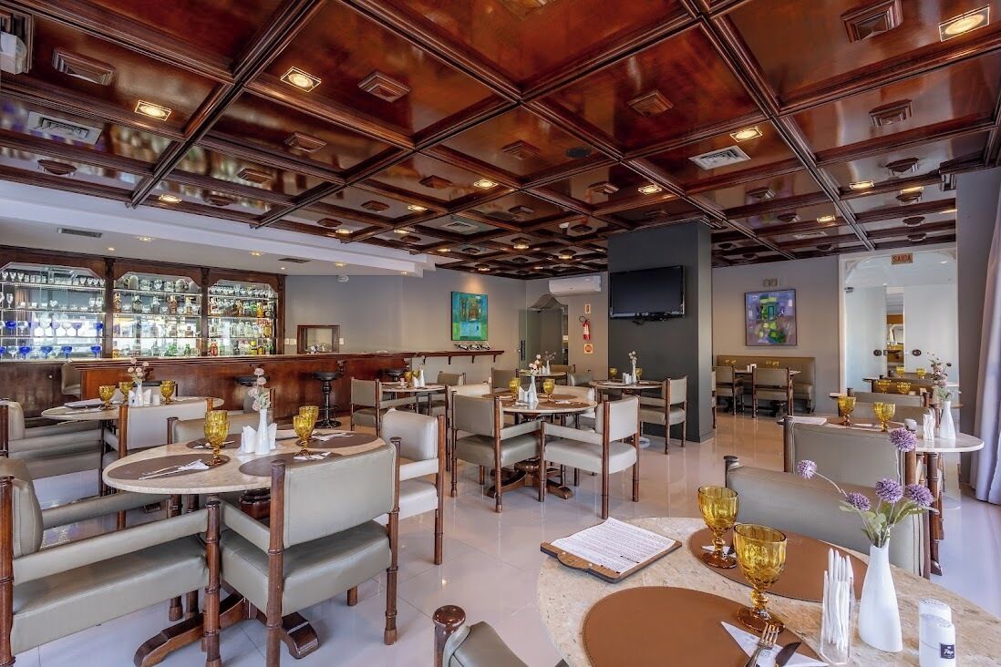 Ein Restaurant mit Holzbalkendecke, mehreren Tischen, Stühlen und einer Bar mit Flaschen.