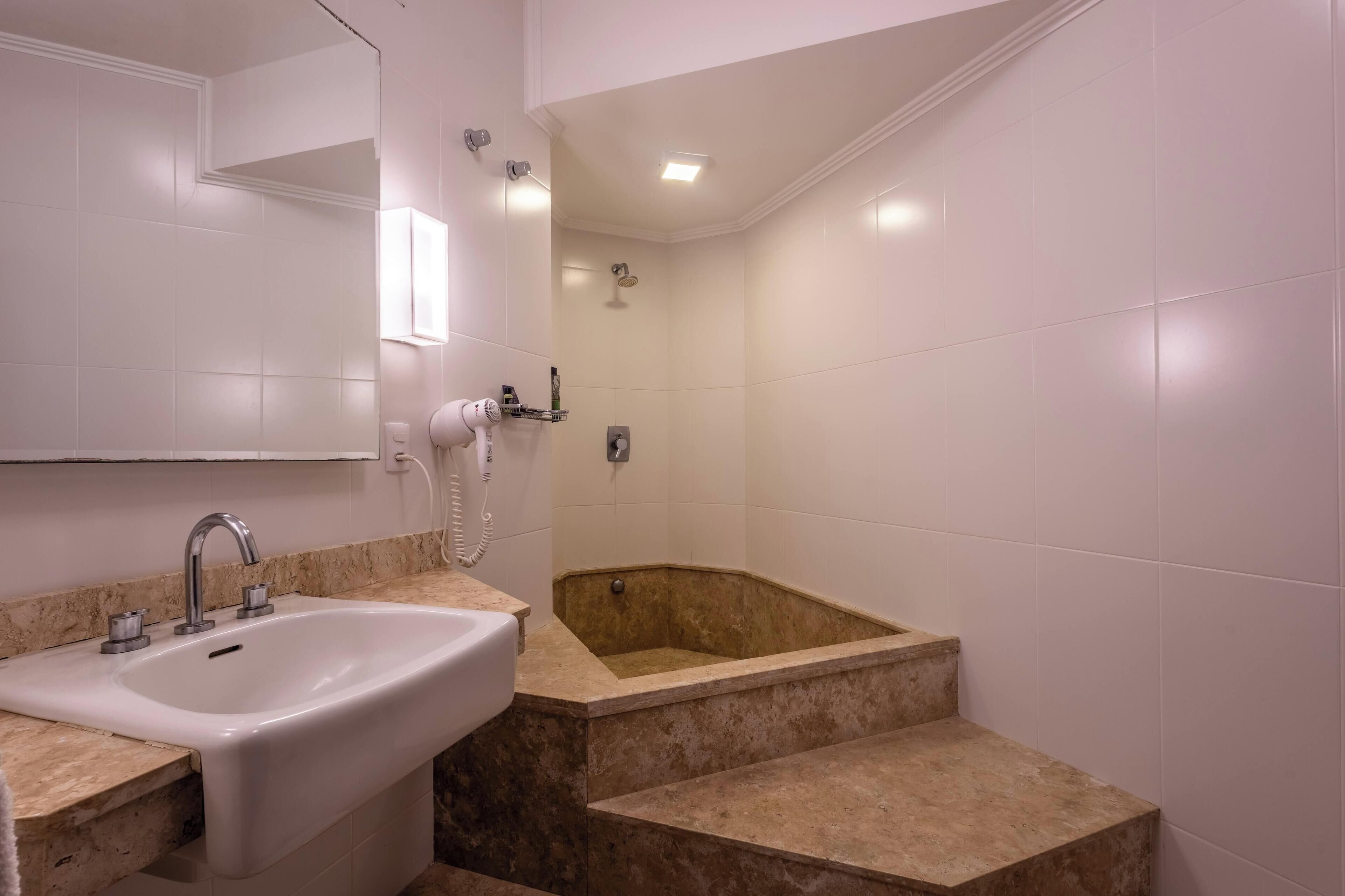 A bathroom with a sink, mirror, and a bathtub with steps leading up to it.