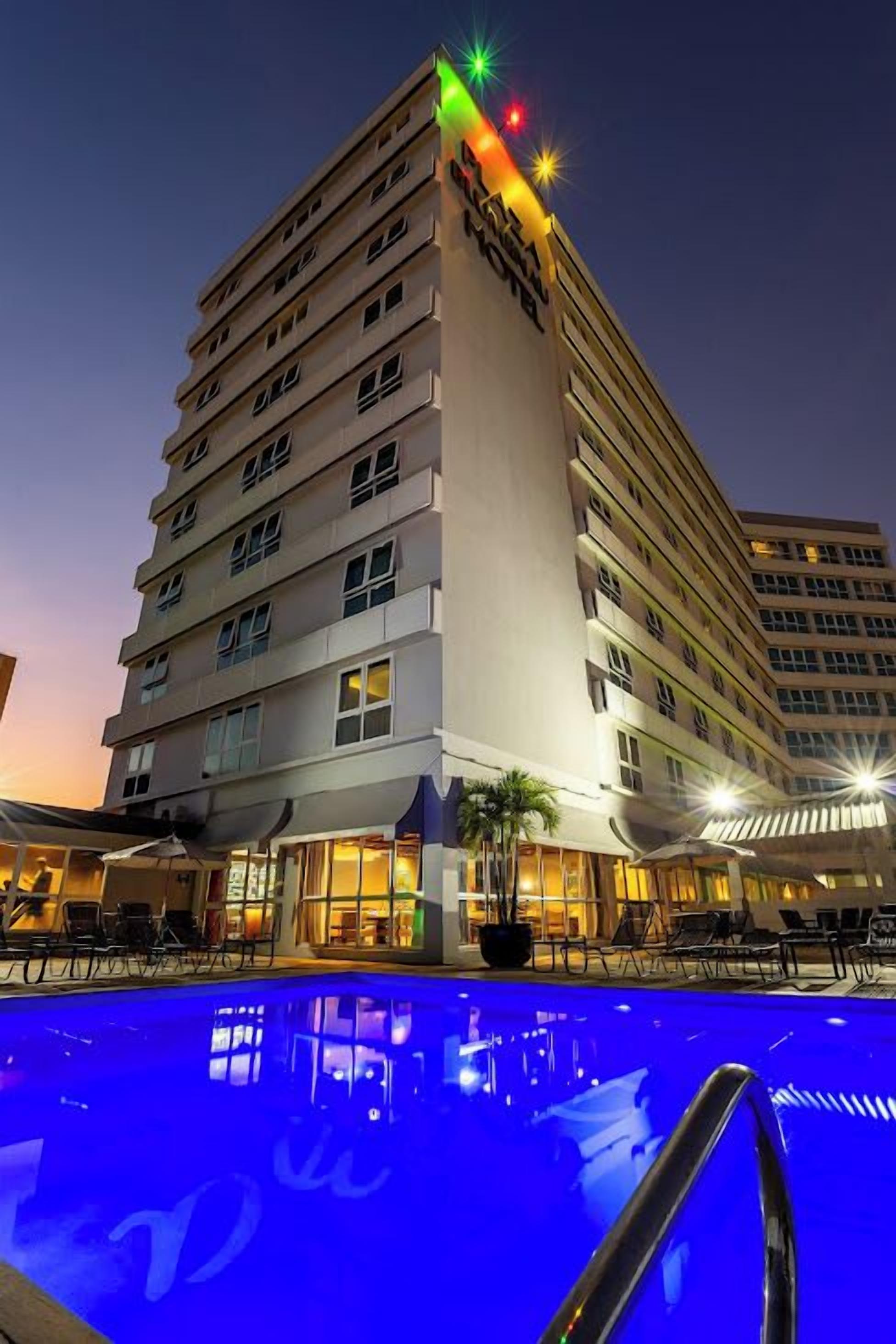 A multi-story hotel with a swimming pool in front, featuring a sign with illuminated letters.