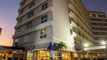 A multi-story hotel with a swimming pool in front, featuring a sign with illuminated letters.