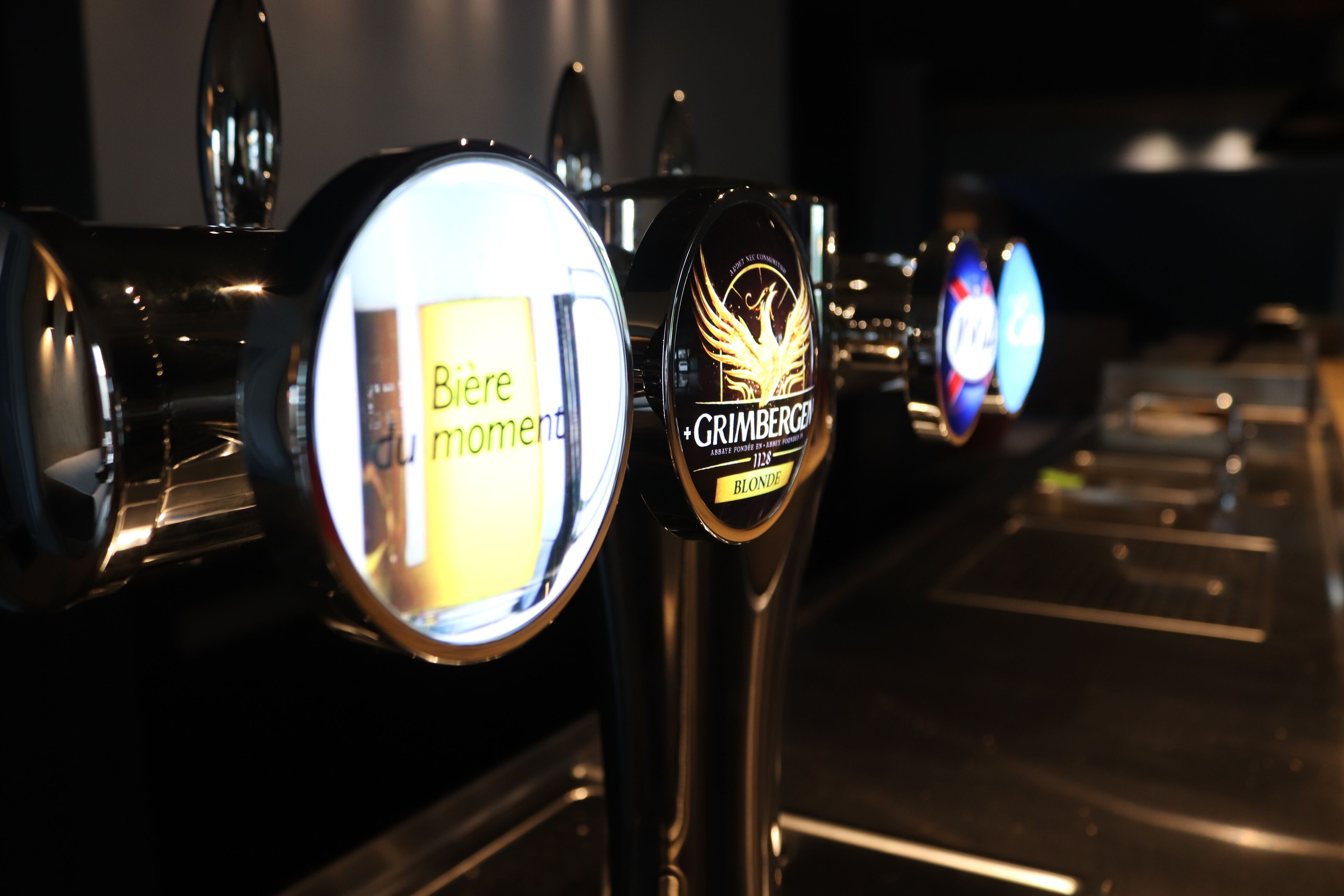 A row of beer taps with labels, including one for 'Grimbergen Blonde'.