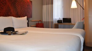 Habitación de hotel con una cama grande, un escritorio con una computadora portátil, una silla, un bolso rojo y una pared con textura.