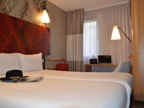 Habitación de hotel con una cama grande, un escritorio con una computadora portátil, una silla, un bolso rojo y una pared con textura.