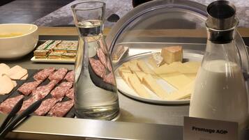 Une présentation de divers fromages, une bouteille de fromage AOP, et un verre d’eau.