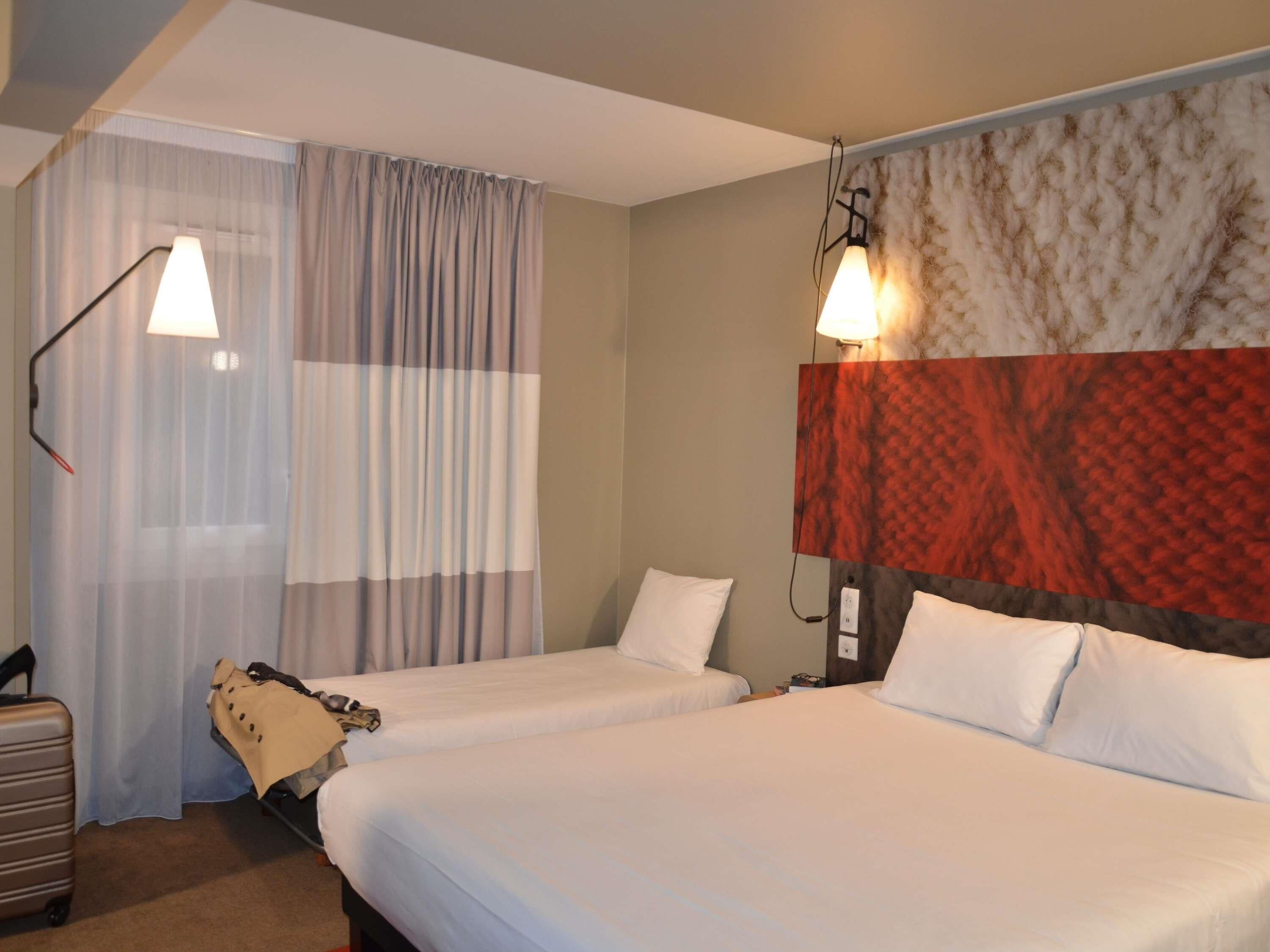 A hotel room with two beds, a suitcase, a lamp, and a patterned wall.