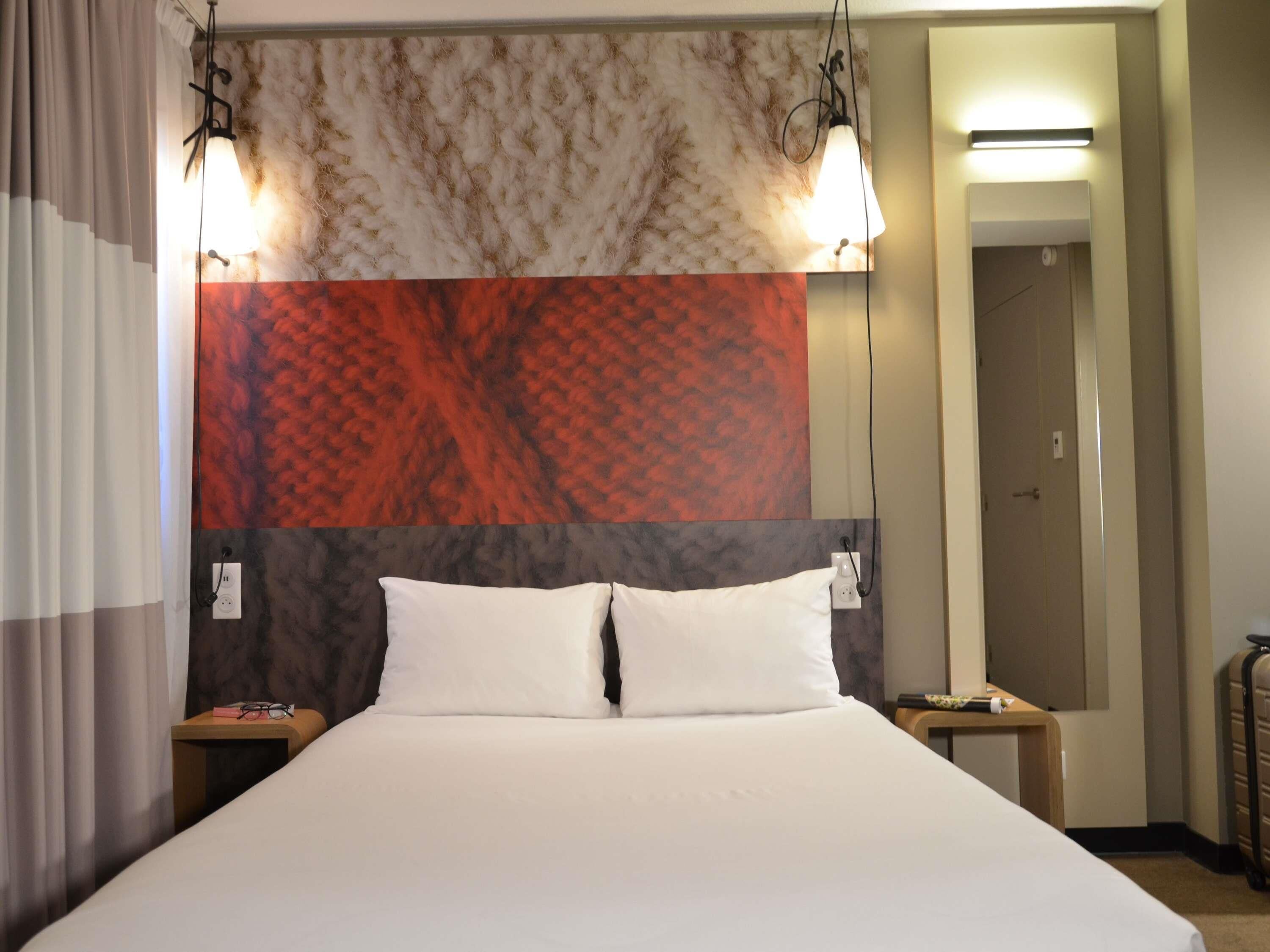 Una habitación de hotel con una cama grande, dos mesitas de noche, un cabecero con diseño estampado y un espejo en la pared.