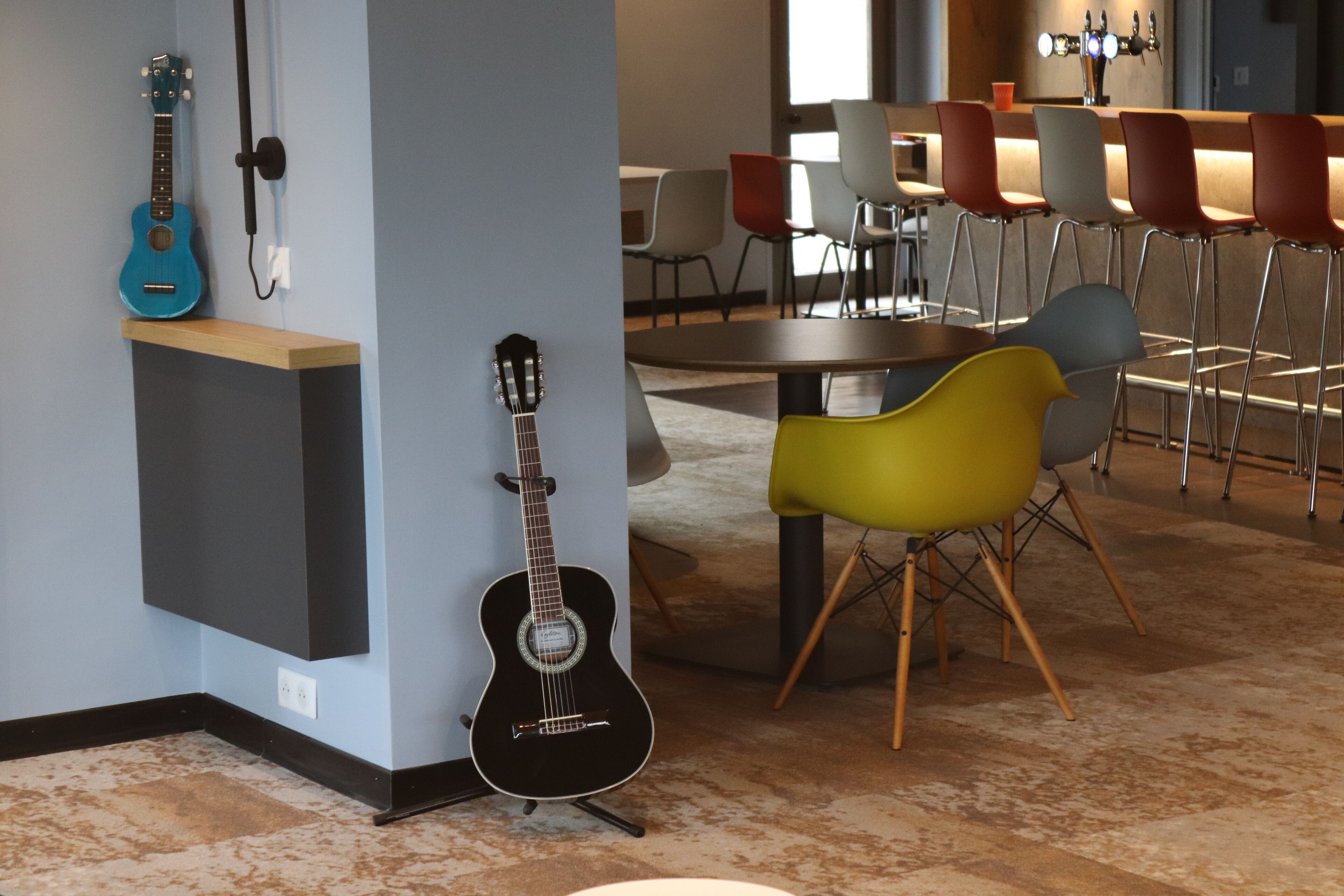 Habitación con dos guitarras sobre un soporte, una mesa con sillas y una zona de bar con taburetes.