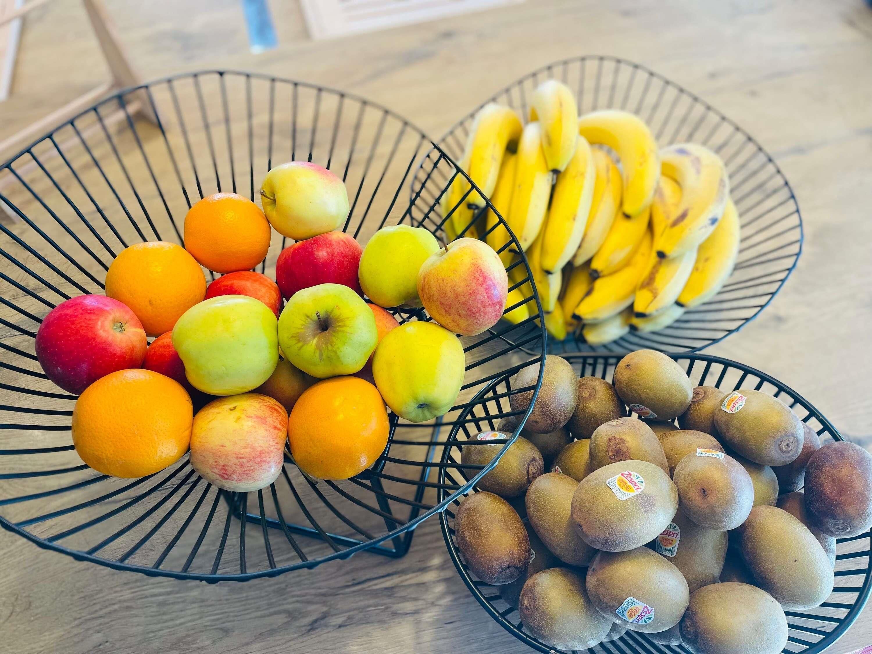 Three wire baskets containing apples, oranges, bananas, and kiwis.