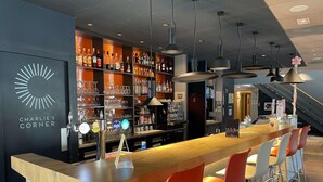 Una zona de bar con mostrador, taburetes y estantes llenos de botellas.