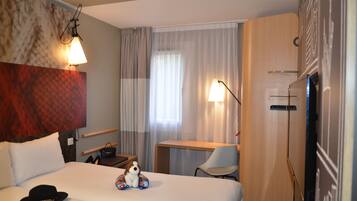 Une chambre d’hôtel équipée d’un lit, d’un bureau, d’une chaise, d’une télévision et d’une lampe fixée au mur.