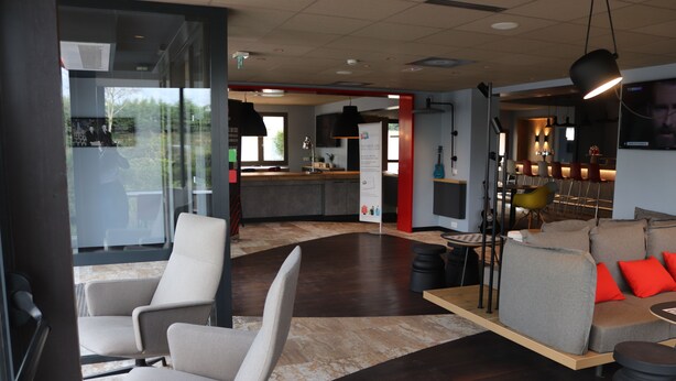 A modern interior with a bar area, seating, and a kitchen in the background. - ibis Melun Hotel (Melun)