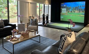 A modern living room with a large TV displaying a golf game, a coffee table with snacks, and a leather sofa.