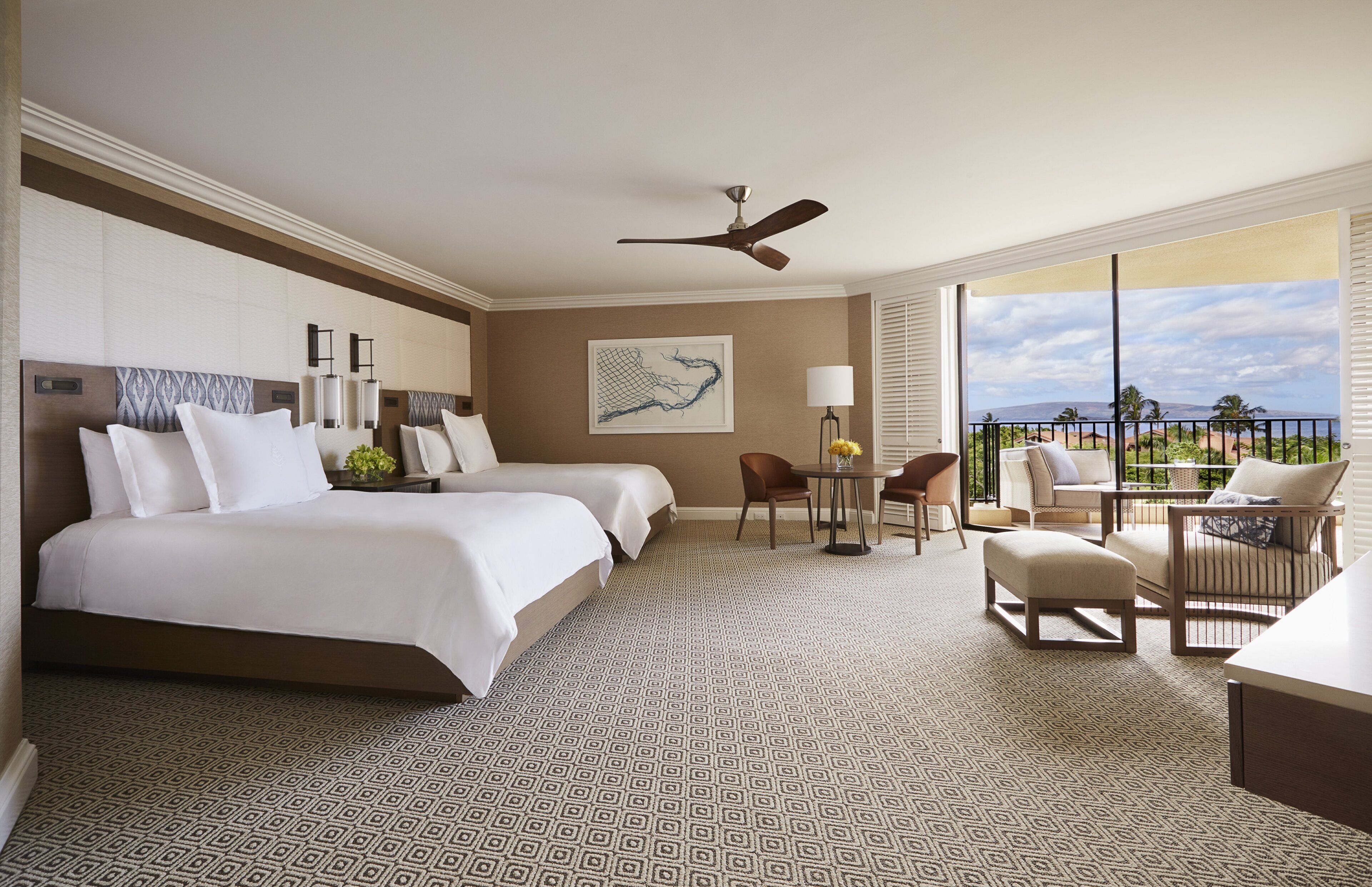 A hotel room with two beds, a dining area with chairs, a table, a ceiling fan, and a large window with a view.