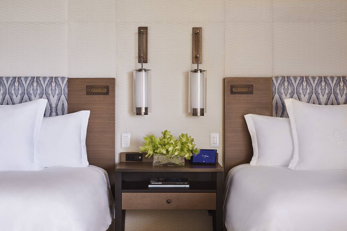 Une chambre d’hôtel avec deux lits, une table de chevet avec une horloge et un vase avec des fleurs.