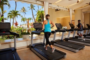 A gym with treadmills, a person running, and a view of palm trees and a building.