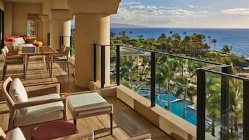 A balcony with wicker furniture, a pool, and a view of the ocean and palm trees.