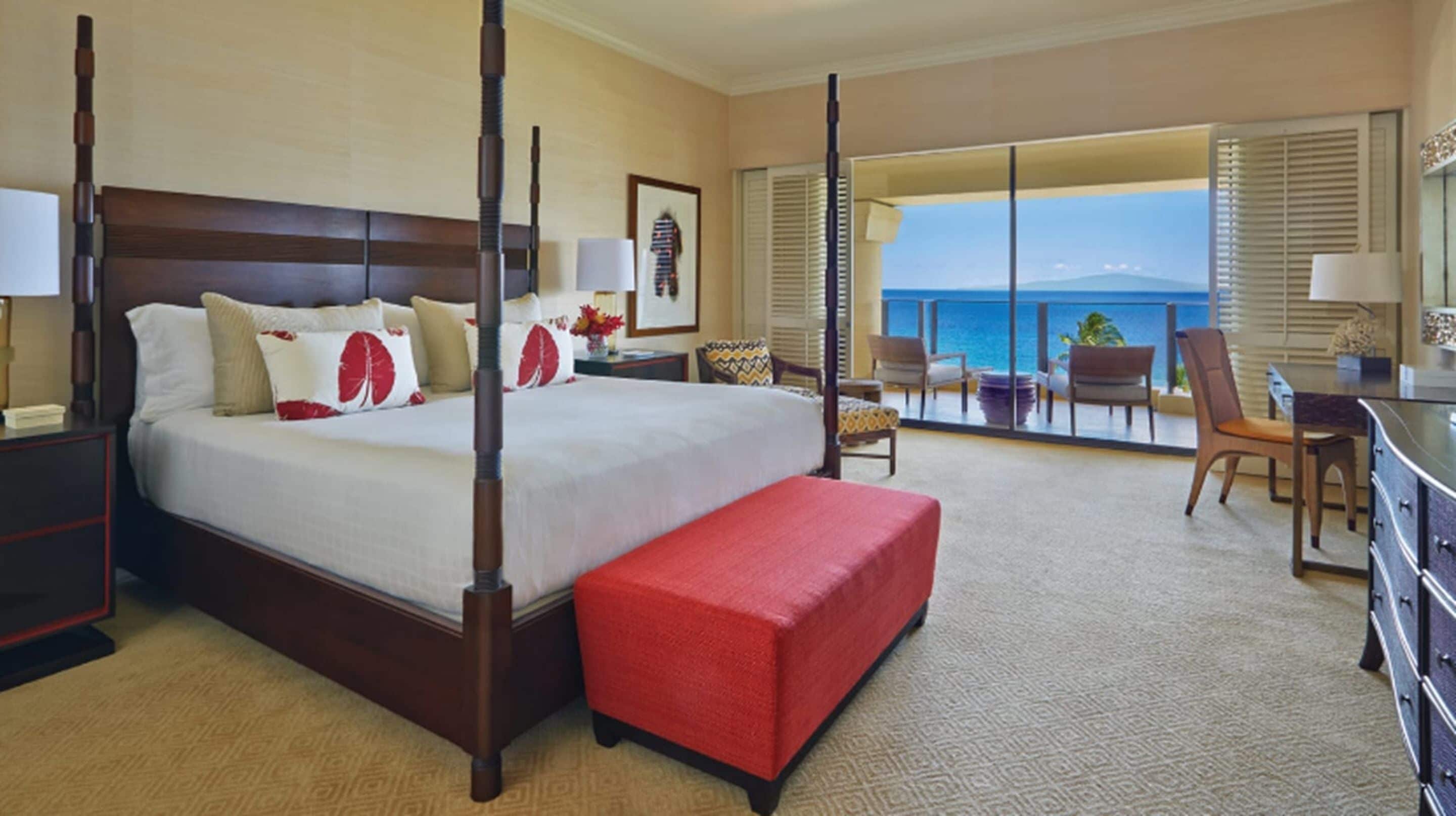A hotel room with a large bed, a balcony with a view of the sea, and a desk with a chair.