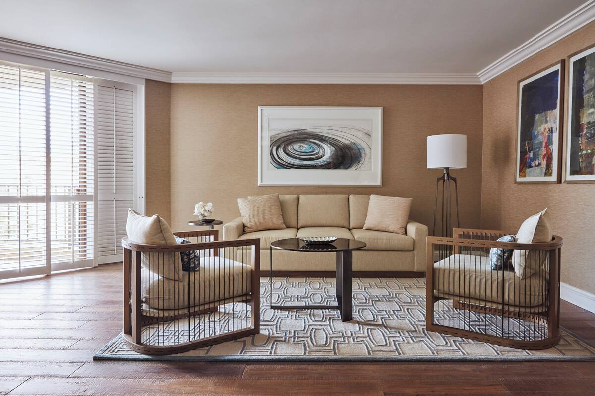 Un salon avec un canapé beige, deux fauteuils en bois, une table basse et un tapis à motifs.