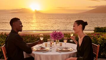 A couple dining at a table with a view of the sunset over the ocean.