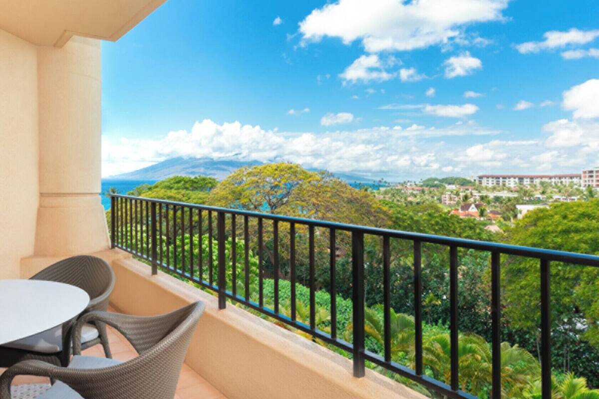 Un balcon doté d’une table et de chaises, offrant une vue sur un paysage luxuriant et des bâtiments éloignés.