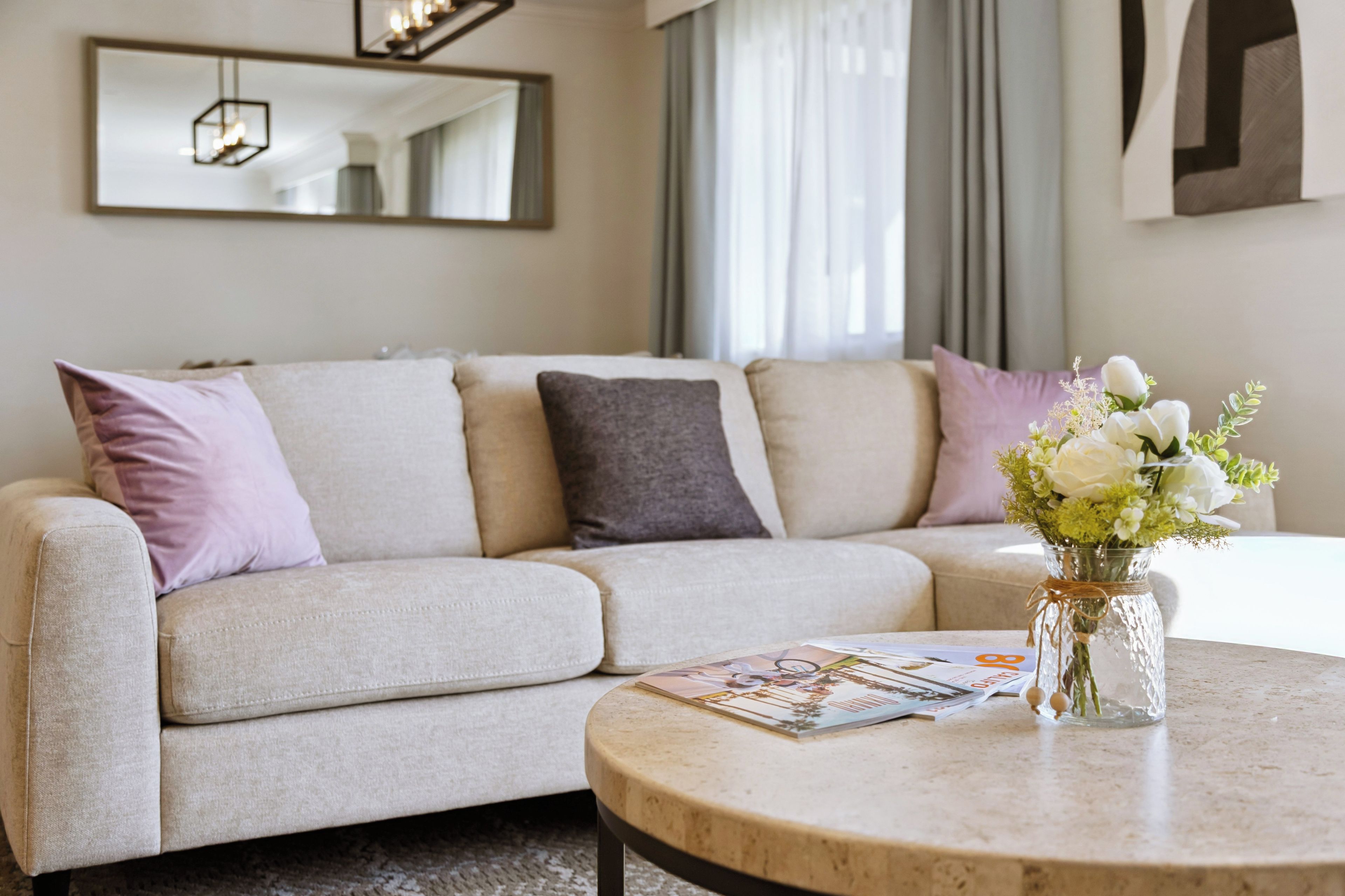 Una sala de estar moderna con un sofá beige, una mesa de centro redonda y un florero con flores.