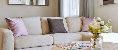 Una sala de estar moderna con un sofá beige, una mesa de centro redonda y un florero con flores.