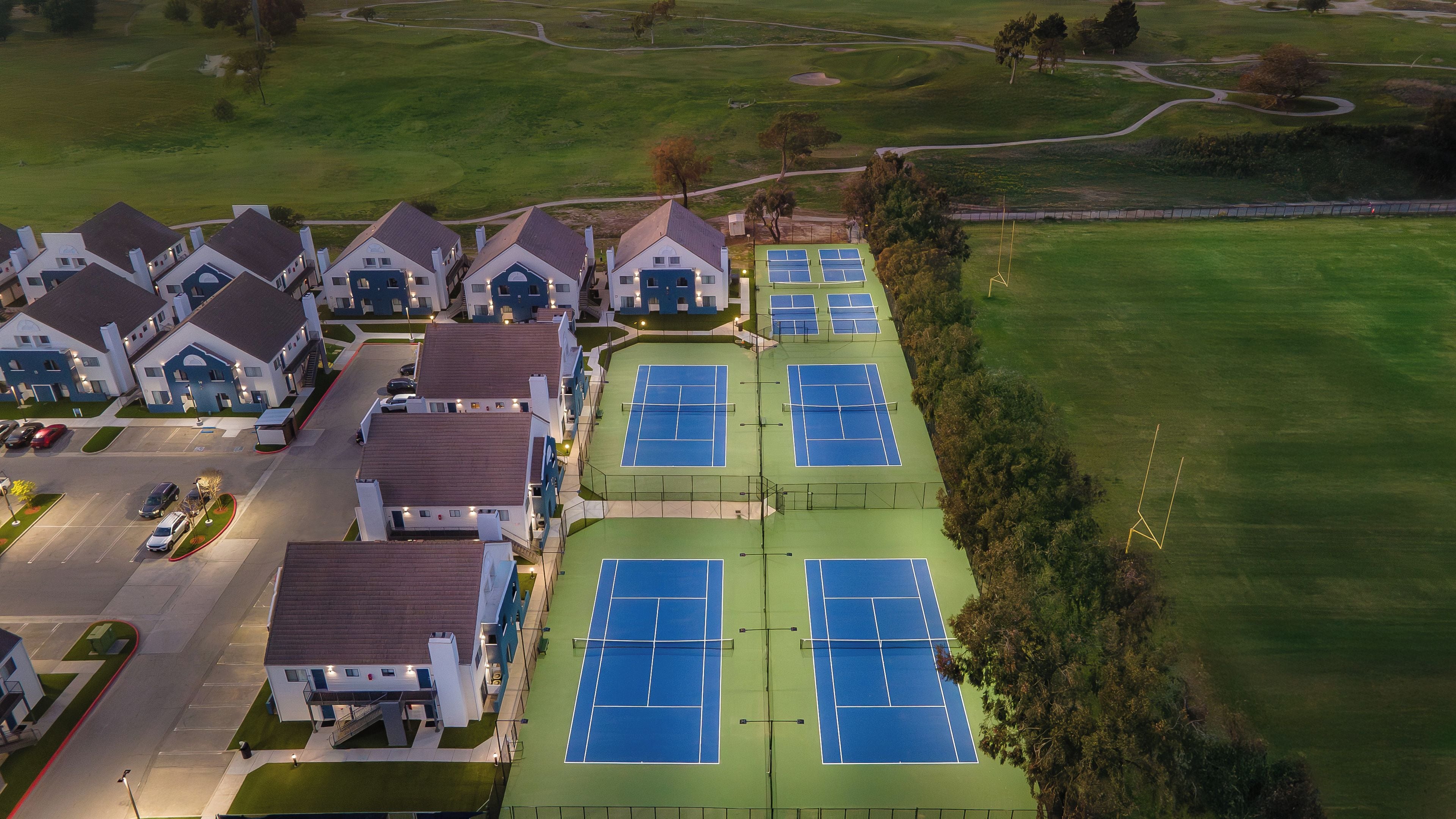 A residential area with multiple houses, a tennis court, and a parking lot.