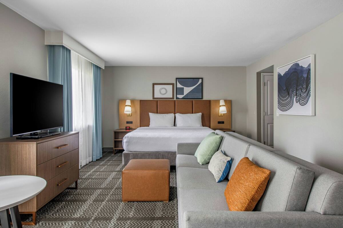 A hotel room with a bed, a TV, a sofa, a desk, and a patterned carpet.