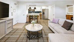A modern living room with a sofa, a coffee table, and a TV. There is a kitchen area with a fridge, oven, and dining table. - Staybridge Suites Oxnard River Ridge by IHG (Oxnard)