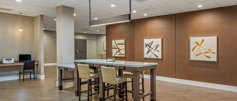 A modern hotel lobby with a long dining table, several chairs, a reception desk, and artwork on the walls.
