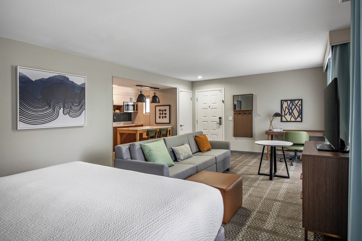 A hotel room with a large bed, a sofa, a desk, and a television.
