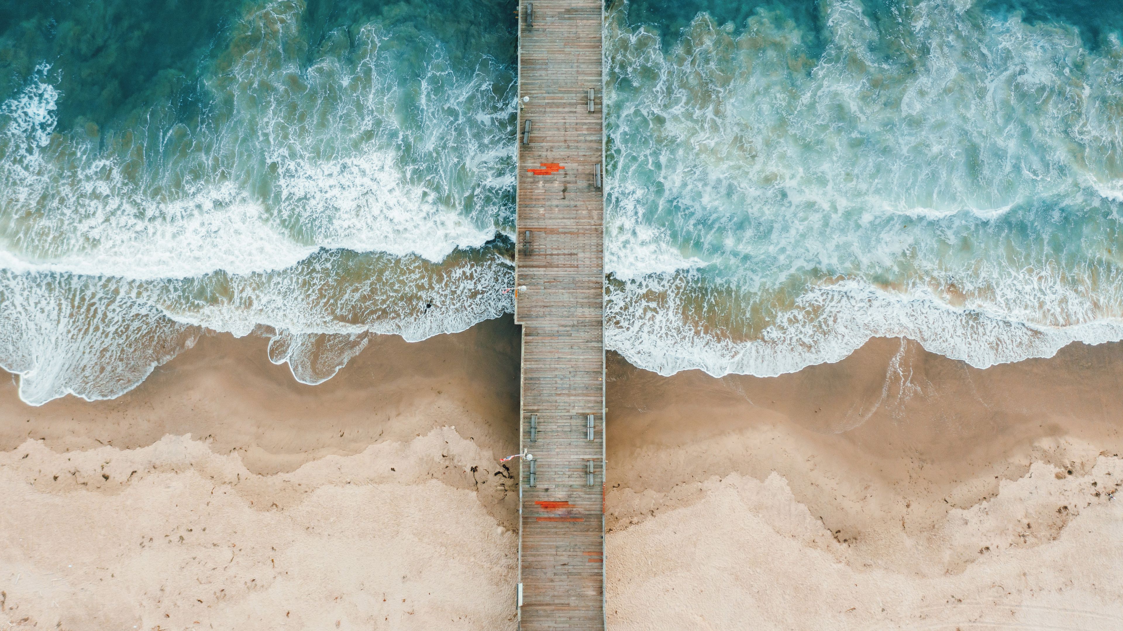 Un muelle de madera que se adentra en una playa arenosa, con olas rompiendo a ambos lados.