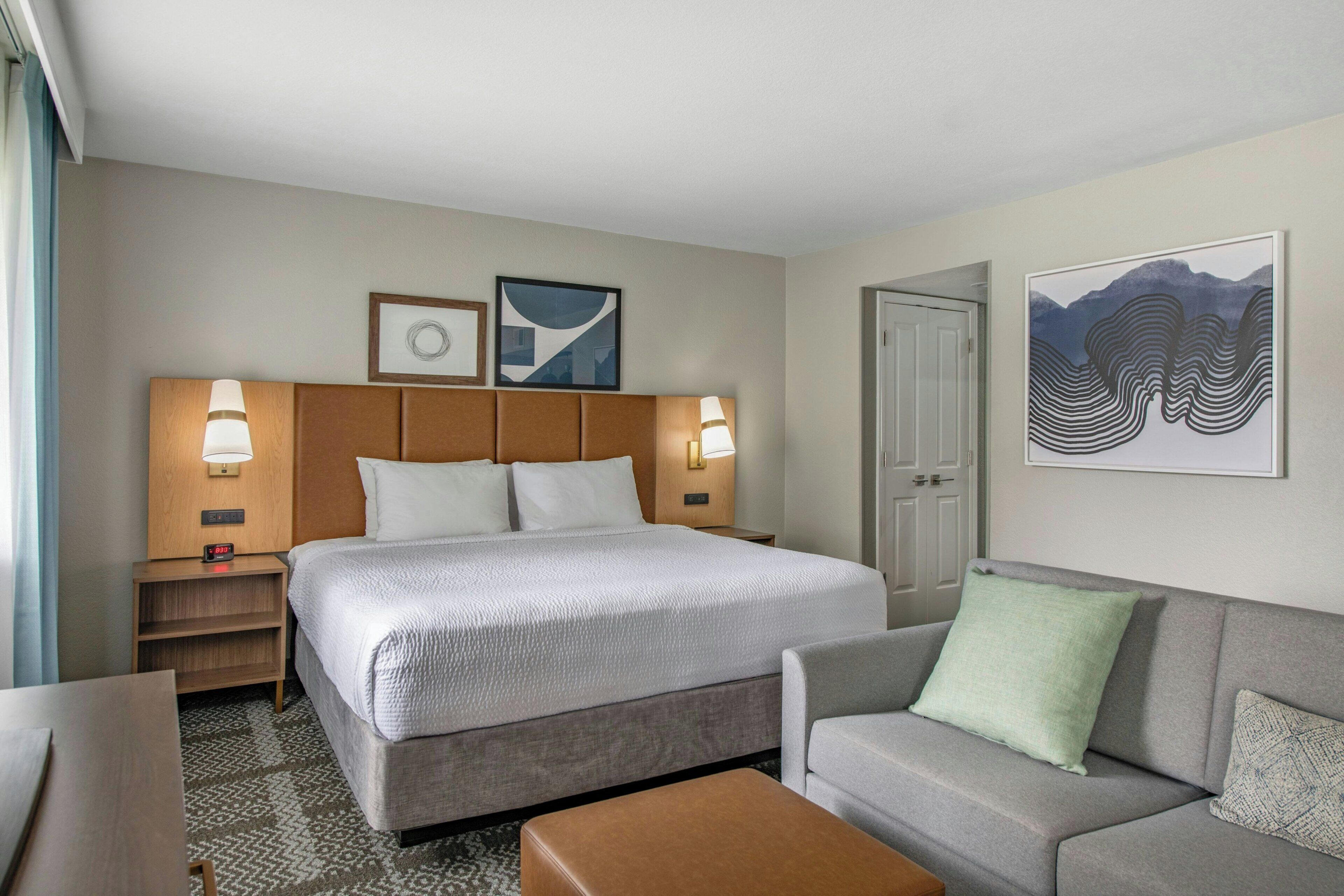 A hotel room with a bed, a sofa, a nightstand, and a door.