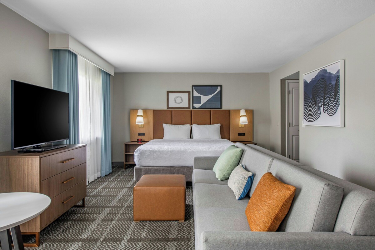 A hotel room with a bed, a TV, a sofa, a desk, and a patterned carpet.