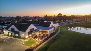 A modern hotel with a large parking lot, a covered outdoor seating area, and a pond. - Staybridge Suites Oxnard River Ridge by IHG (Oxnard)