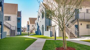 A modern apartment complex with multiple buildings, a central tree, and a well-maintained lawn.