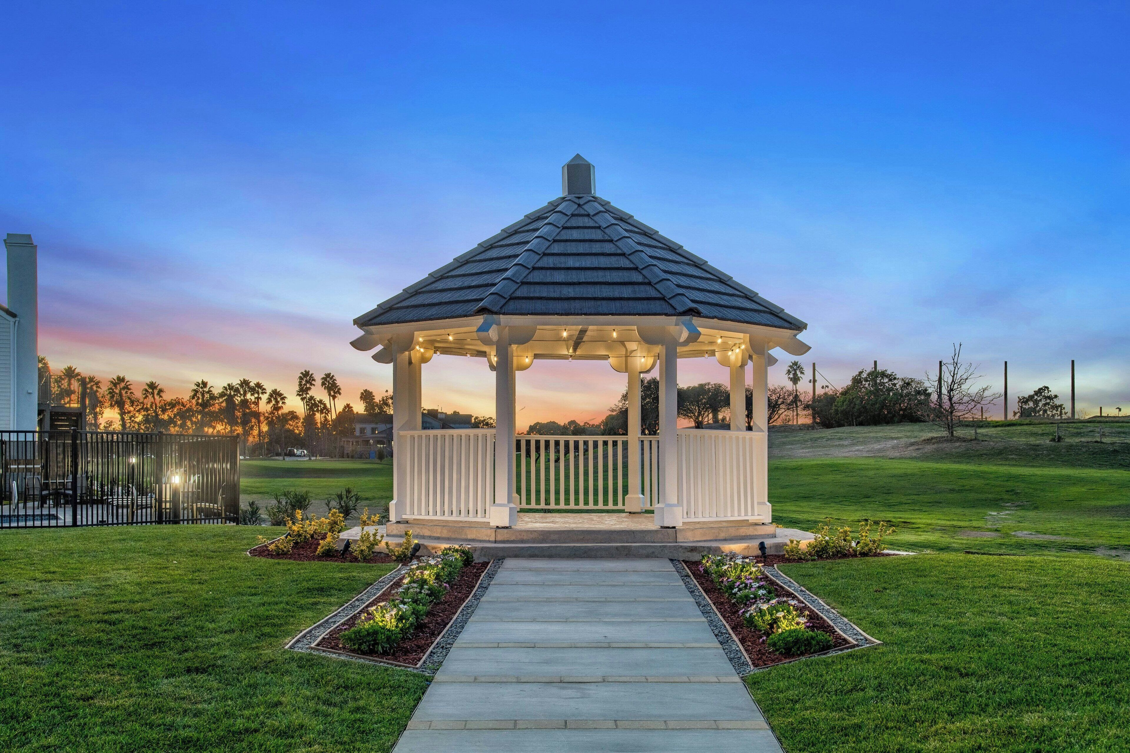 A gazebo with a tiled roof, surrounded by a well-maintained lawn and a pathway leading to it.