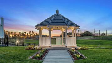 A gazebo with a tiled roof, surrounded by a well-maintained lawn and a pathway leading to it.