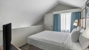 A hotel room with a bed, a television, a desk, and a window with curtains.