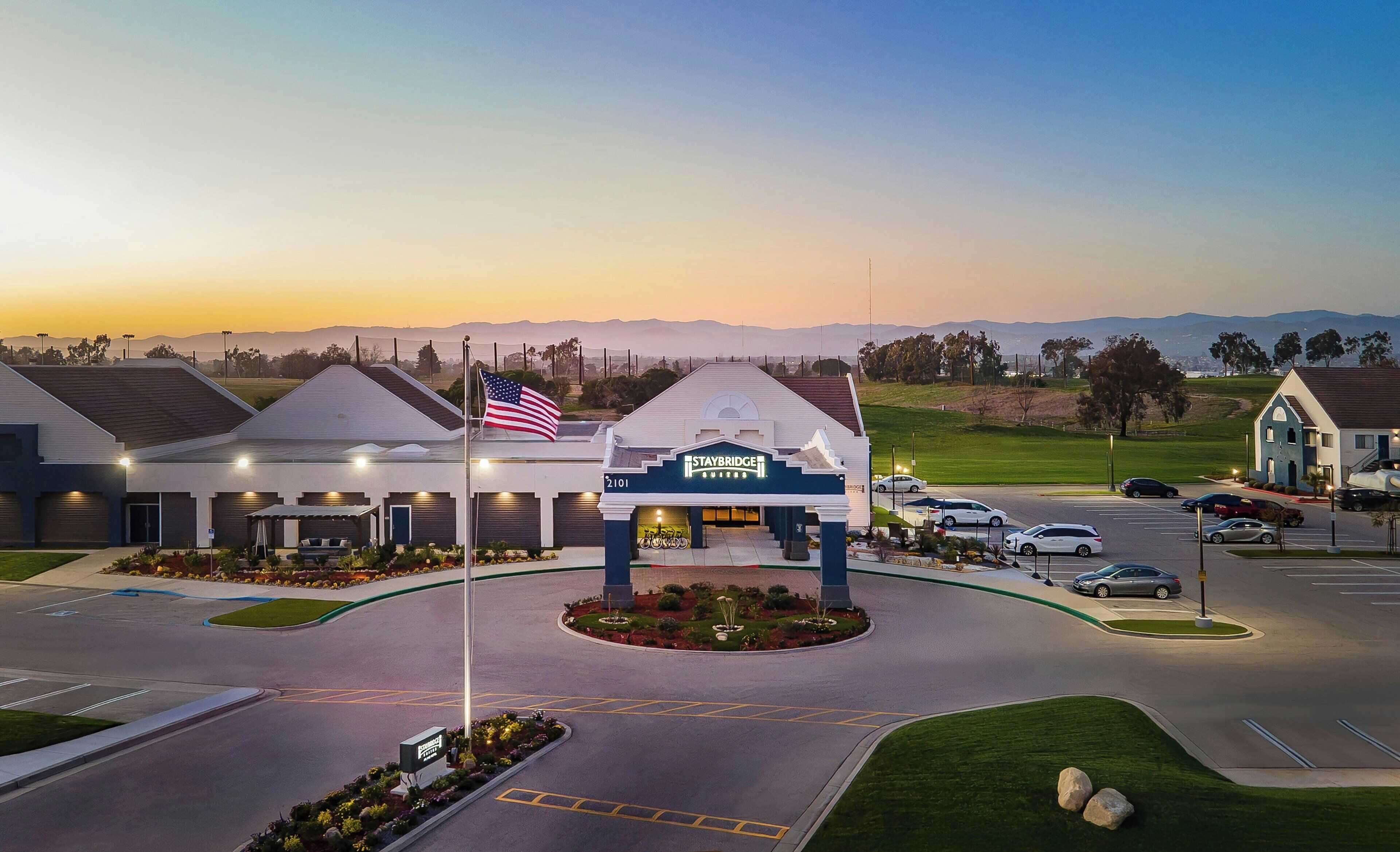 A Staybridge Inn with a prominent American flag, a parking lot, and a view of distant mountains.