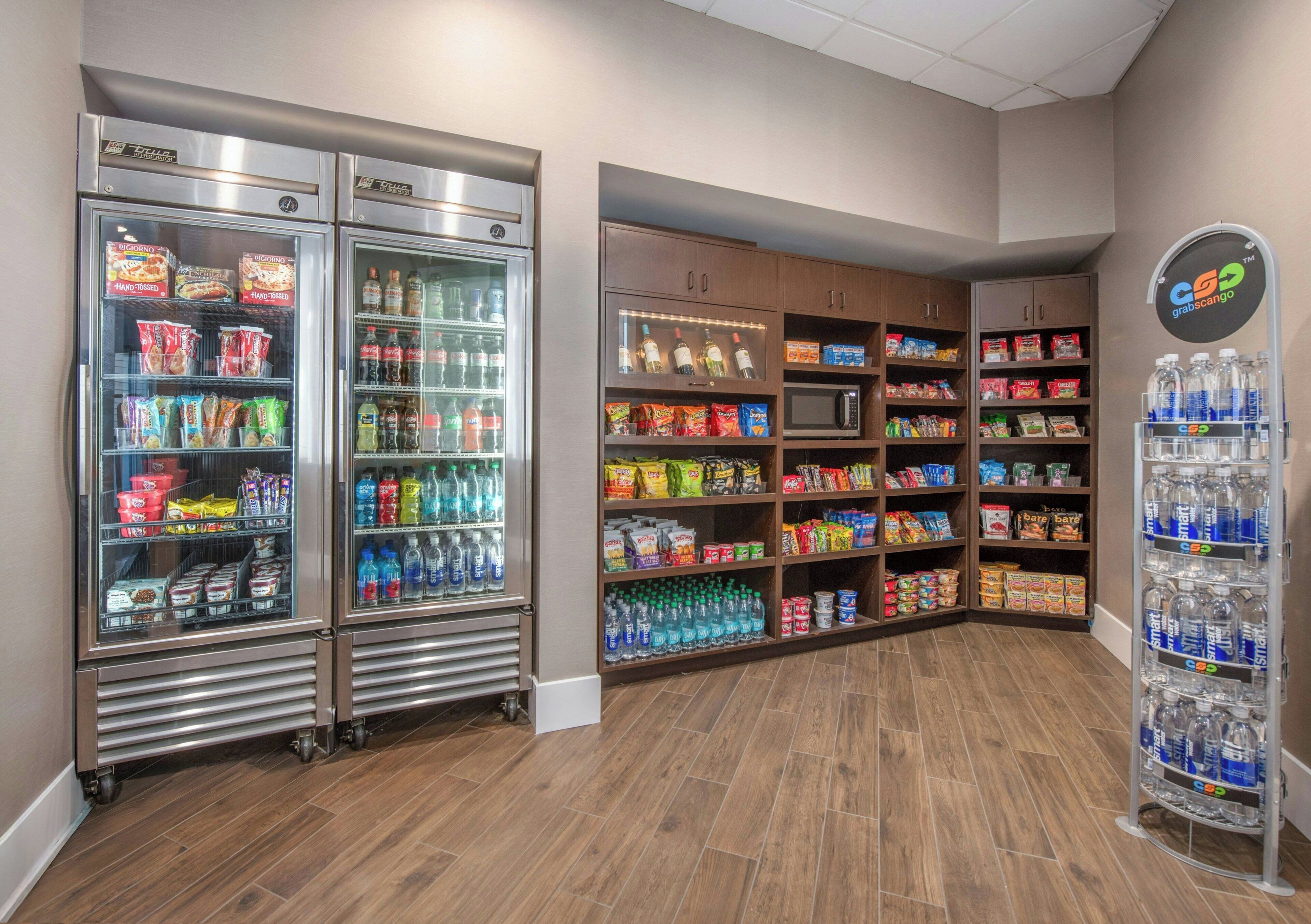A self-service beverage station with refrigerated and non-refrigerated options, a microwave, and shelves stocked with snacks and beverages.