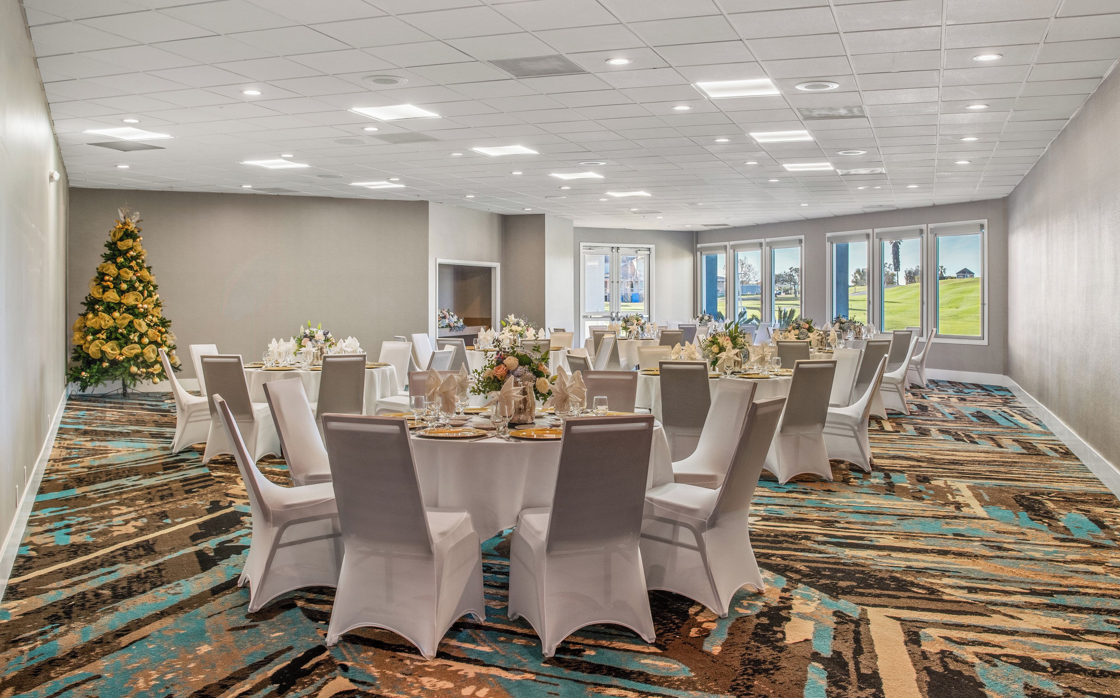 A banquet hall with round tables, white chairs, and a Christmas tree.